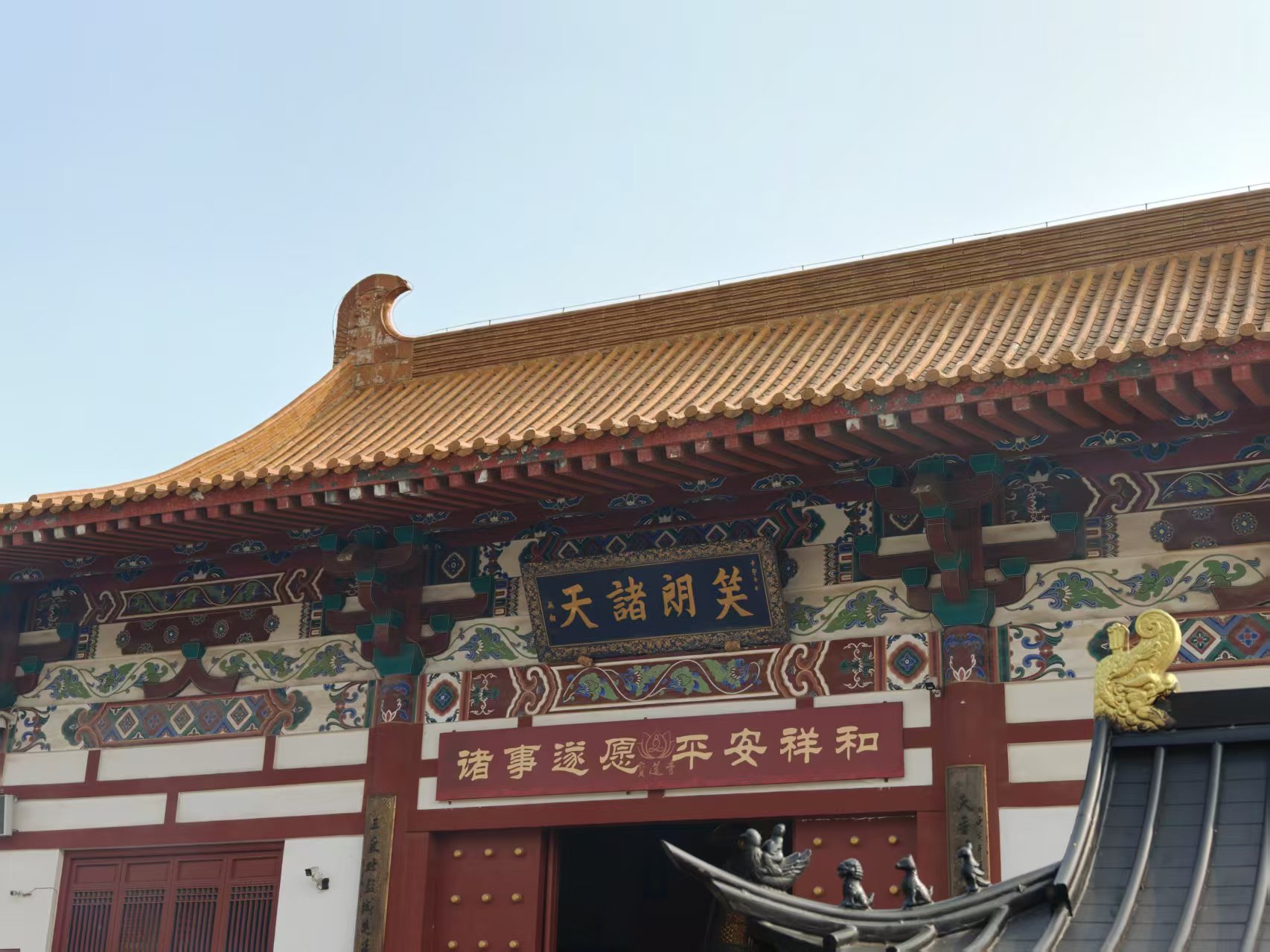 红墙大殿上的两块牌匾,上匾写着笑朗诸天,下匾写着诸事遂愿 平安祥和,檐角金黄琉璃瓦