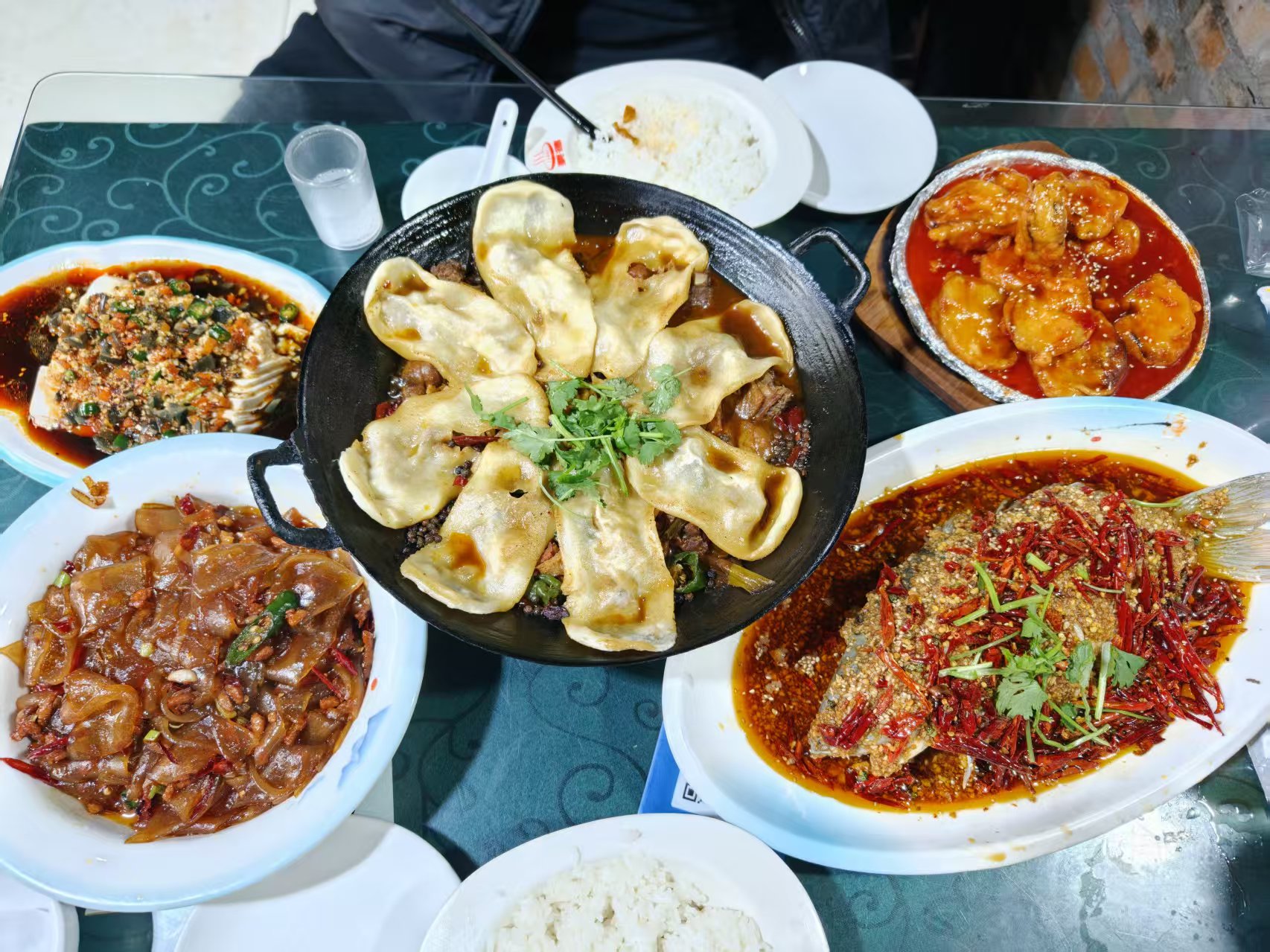 绿桌布上的聚餐:黑色铁锅炖菜贴一圈面饼,油泼鱼铺满干辣椒和香菜,还有皮蛋豆腐