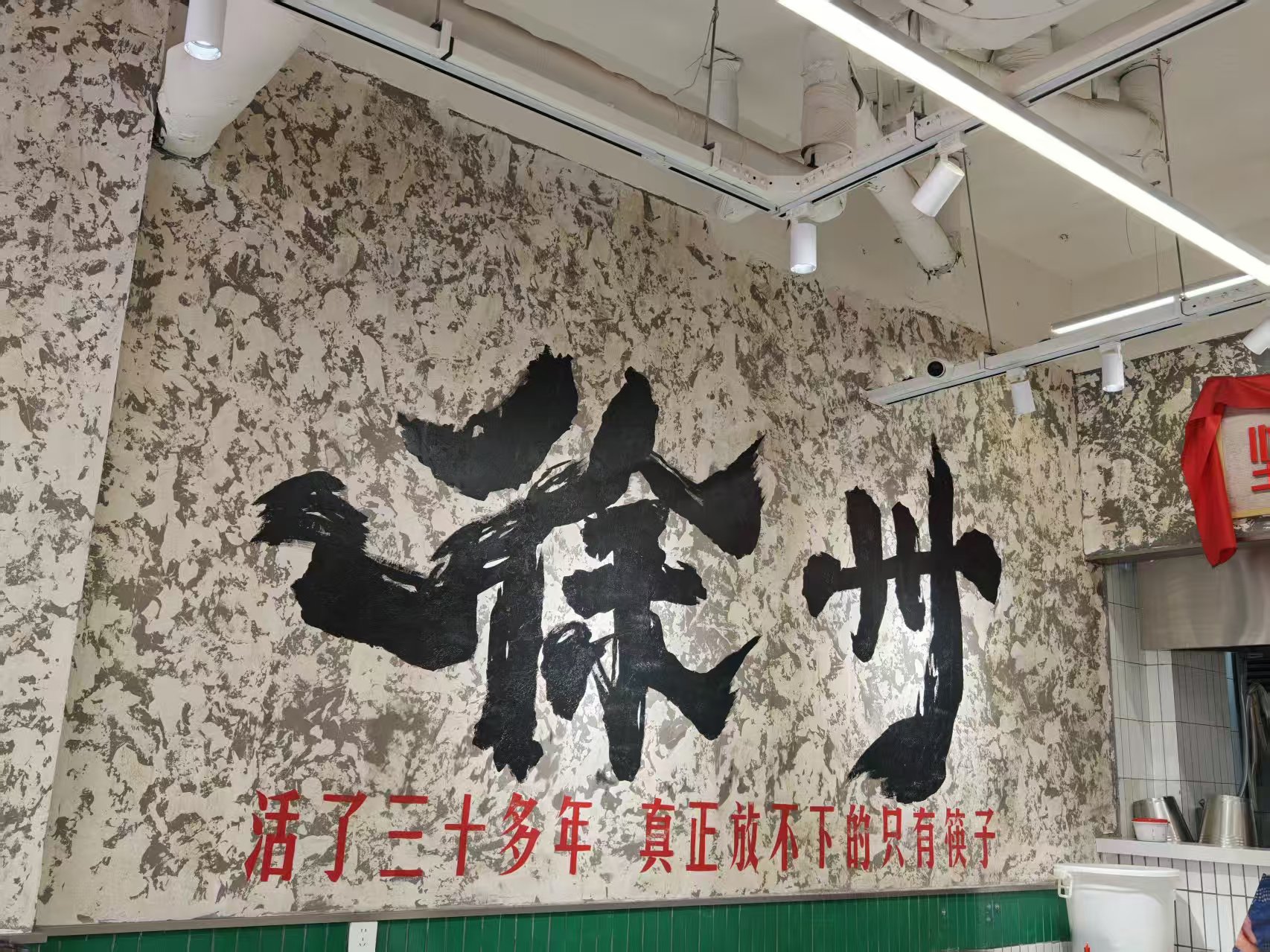 餐饮门店做旧墙面上巨大的黑色书法字徐州,下方红字写着活了三十多年 真正放不下的只有筷子